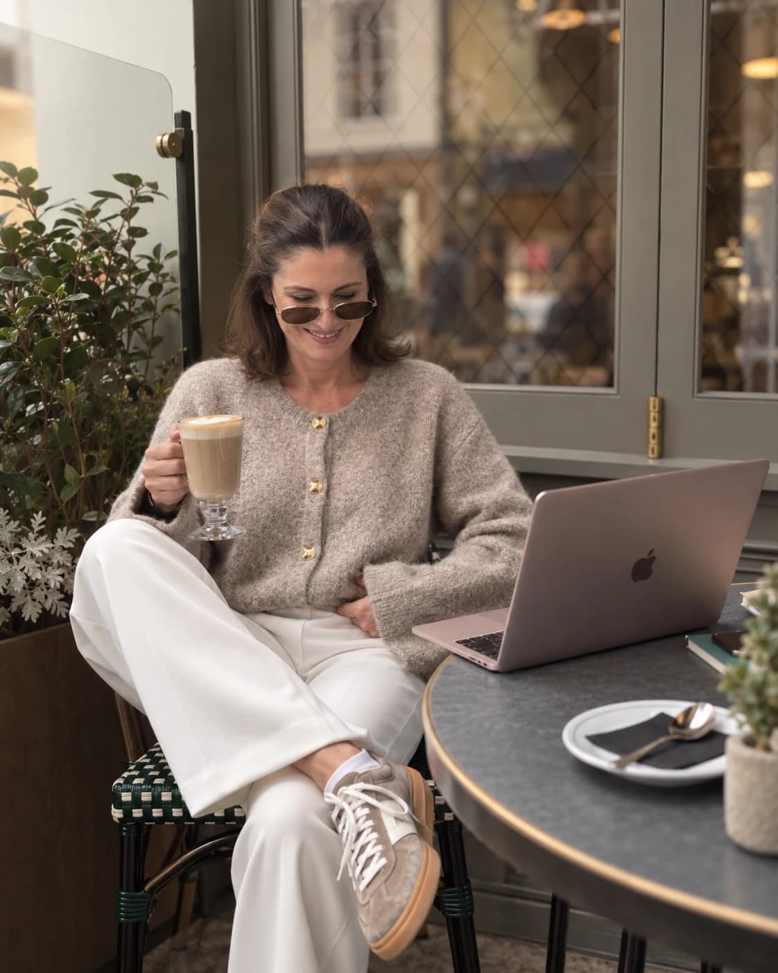 Linda Cunningham smiling with a latte at a café table, her laptop open beside her