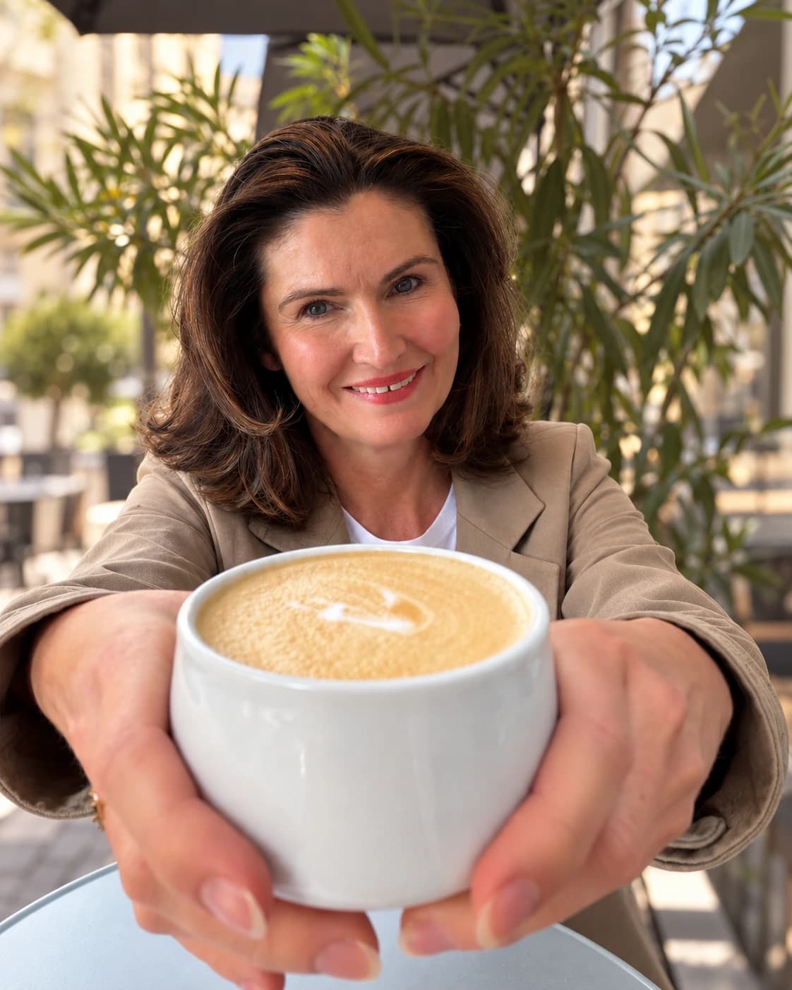 Linda Cunningham smiling at a café table, holding a flat white towards the camera